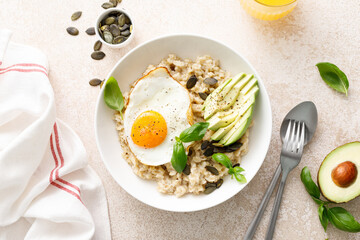 Savory oatmeal with fried sunny side up egg, avocado and pumpkin seeds for healthy breakfast