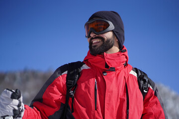 Close-up photo of smiling young man wearing ski equipment cap, goggles and gloves. Happy man skiing...