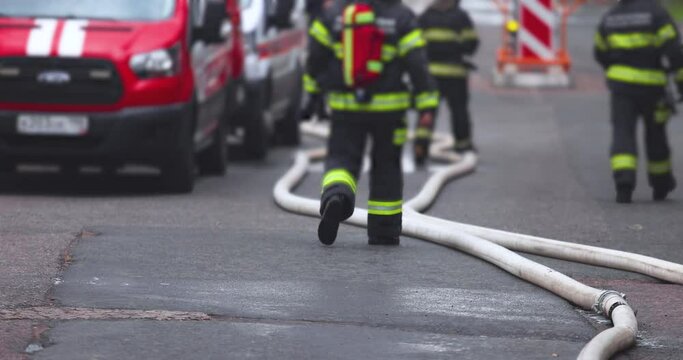 Group of fire men in uniform during blaze, fire fighting operation in the city streets, firefighters with the fire engine truck fighting vehicle in the background, emergency and rescue, slow motion