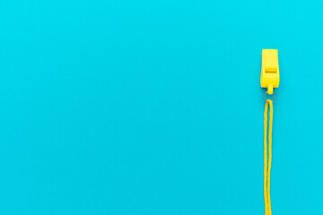 Plastic referee whistle on turquoise blue background with copy space. Flat lay image of yellow referee whistle.