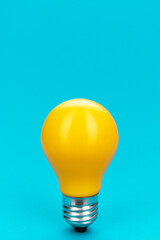 Yellow bulb standing on turquoise background with copy space. Minimalist photo of lightbulb over blue.
