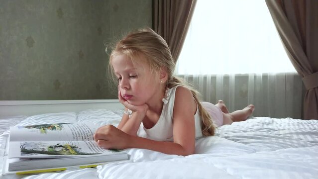 Little cute girl lying in the bed with a book. Concept of education at home