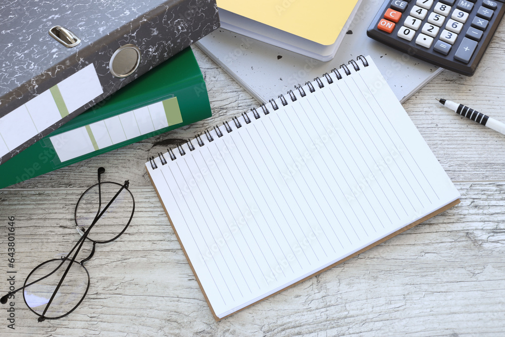 Poster top view of a blank notepad with glasses, a calculator and a folder on a wooden table. close-up