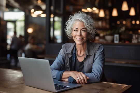 Middle-aged old woman working on laptop sitting in cafe and smiling at camera. Mature businesswoman, female entrepreneur, female business owner. Generative AI