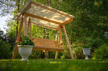 Wooden garden swing in the morning sun. Morning relaxation in nature. Landscape design on a country...