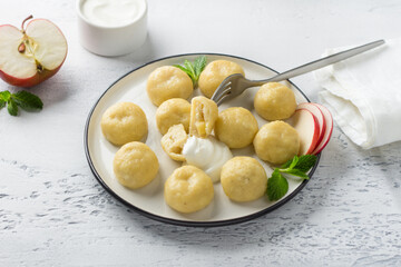 Vegetarian gluten-free steamed lazy dumplings with apple filling on white plate, decorated with mint surrounded by half an apple and sour cream on light gray background