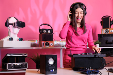 Cheerful musician standing at dj table mixing electronic music with techno using professional mixer...