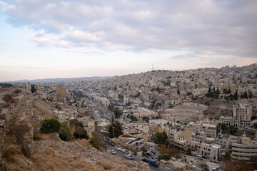 Cityscape of Amman, as seen from the Amman Citadel. Houses are built over the sloping hillside, in the center of which is the ruin of the enormous Roman Theatre, showing a mix of old and new elements.