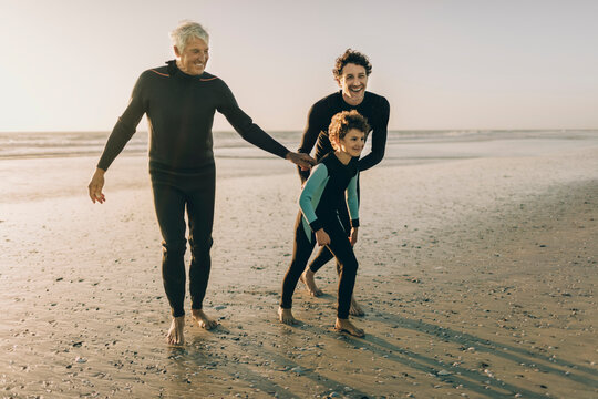 Multigenerational family of male surfers getting ready to surf on a sandy beach