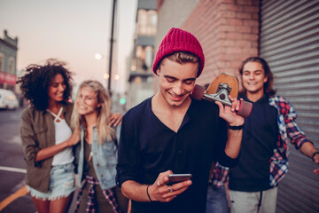 Young caucasian man using a smart phone while out with his friends in the city