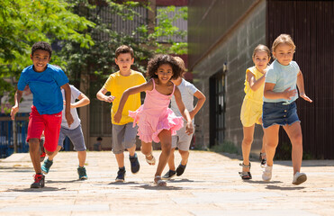 Obraz premium Team of positive kids running in race in the street and laughing outdoors