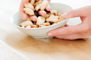 Nuts. Brazil nuts in a white ceramic cup in hand on a wooden table. Healthy fats in the diet. hand takes brazil nuts from a plate close-up.Useful healthy snack. Brazil nuts in the diet.