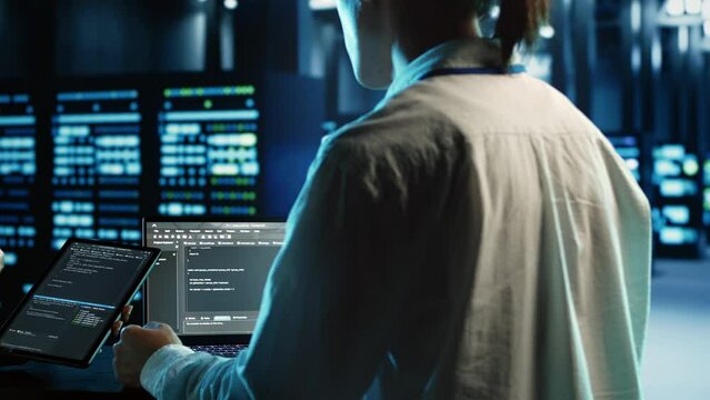 Engineering team members running code on tablet and laptop, updating professional data center equipment designed to accommodate server rigs, networking systems and storage arrays