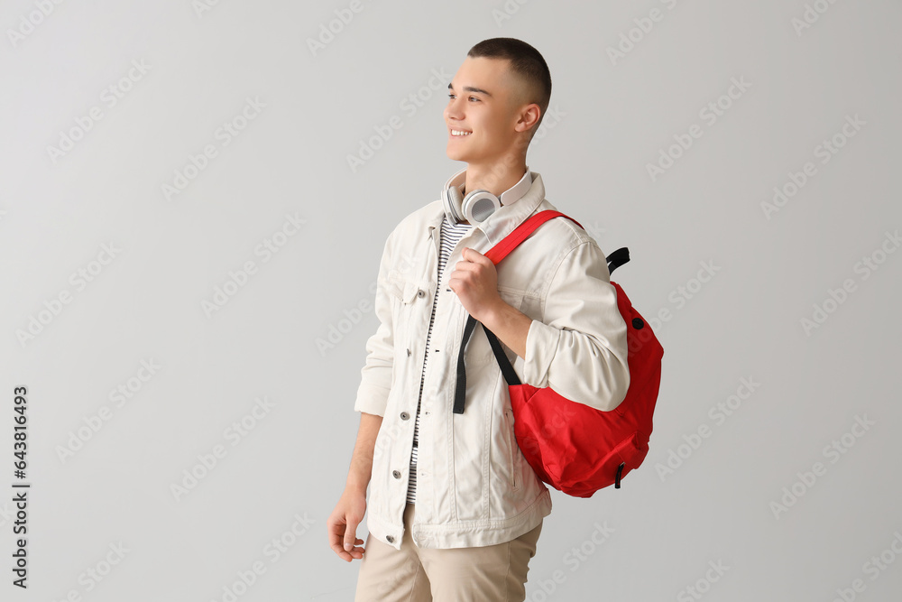 Poster male student with backpack and headphones on grey background