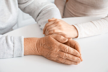 Fototapeta premium Young woman with her grandmother holding hands at table in kitchen, closeup