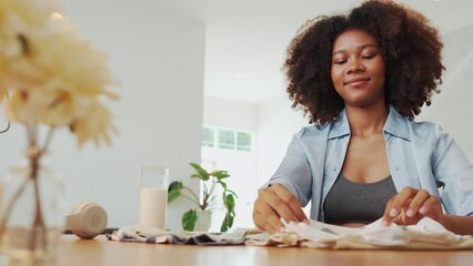 Happy Black African American Pregnant woman in curly hair looking at baby clothes while packing her clothing and getting ready for maternity hospital. Expecting mother at home. Pregnancy. Motherhood.
