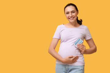 Young pregnant woman with Folic Acid pills on yellow background