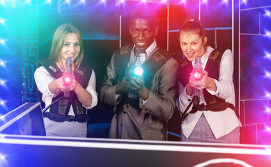 African male and two adult caucasian women holding laser guns and posing at laser tag room