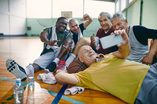 Diverse group of seniors taking a selfie on a smartphone after playing basketball in a indoor basketball gym
