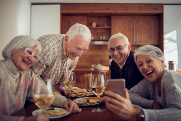 Group of senior people using a smartphone while having lunch together in the dining room at home