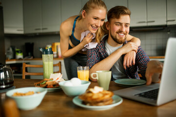 Young couple having breakfast and using a laptop after a exercise in the kitchen