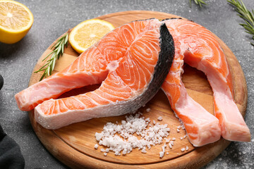 Wooden board with raw salmon steaks and different spices on grey background
