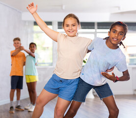 Interested modern tweens, smiling dark-skinned boy and european girl learning to dance waltz as...