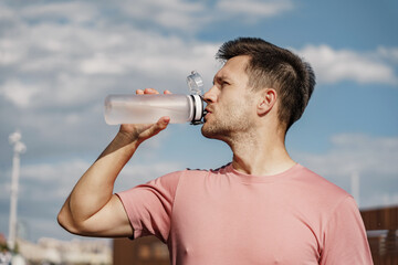 A man drinks water from a sports bottle. The athlete is a confident person in fitness clothes, a strong young coach doing exercises for running.