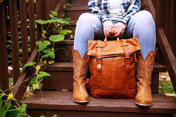 woman is holding a brown leather backpack while sitting on the steps. Close-up of hands and leather...
