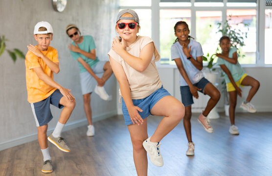 Smiling cute tween girl performing krump movements with group in dance studio. Form of artistic expression of modern children..