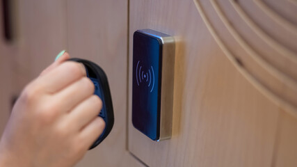 A woman opens the electronic lock of a cubicle in a locker room with a bracelet. 
