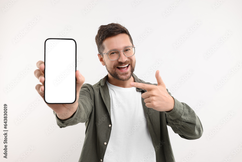 Poster handsome man showing smartphone in hand and pointing at it on white background