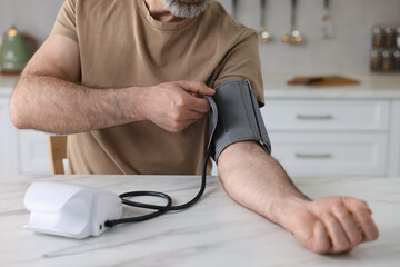 Man measuring blood pressure at table indoors, closeup