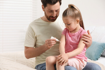 Father applying ointment onto his daughter's arm on bed indoors