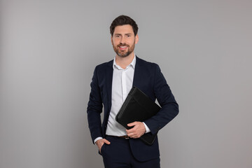 Happy real estate agent with leather portfolio on grey background