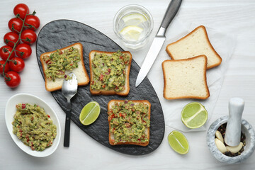 Delicious sandwiches with guacamole and ingredients on white wooden table, flat lay
