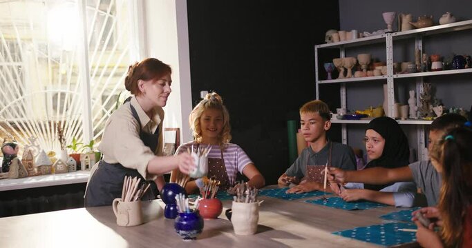 Teacher gives shaper sticks for pottery to smiling students