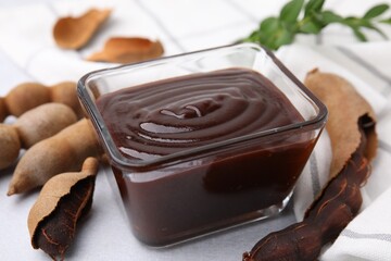 Bowl of tasty tamarind sauce and fresh pods on light table, closeup