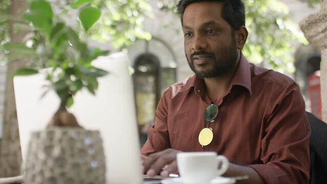 Handheld shot of casual male working on his laptop at an outdoor cafe