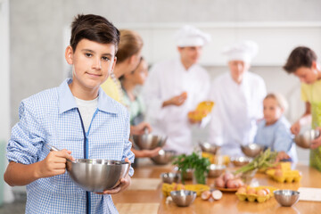 Cooking course - portrait of teenage boy in an apron who is learning to beat eggs to make pancakes...