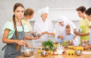 Cooking course - portrait of a girl in an apron who is learning to beat eggs to make pancakes at a cooking class