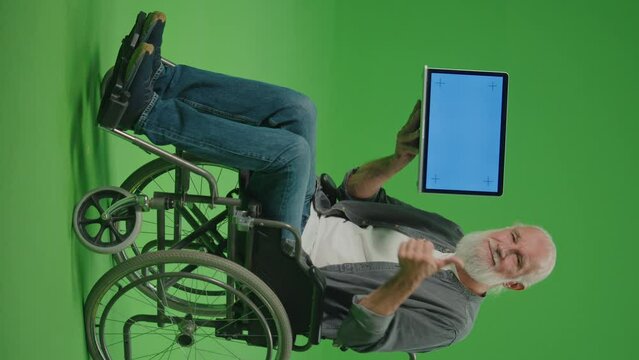 Vertical View. Green Screen.Portrait of an Old Man in a Wheelchair with a Laptop with Blue Screen Shows Thumps Up.Community and Social Support for Elderly People in Wheelchairs.