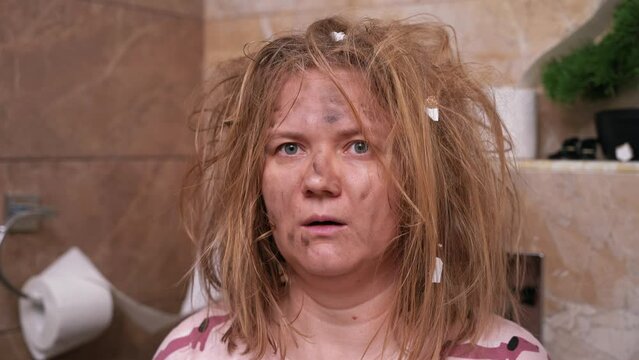 Portrait of woman with tousled matted hair, face smeared with soot sits surprised in toilet blinks in shock. Silly April Fools jokes, childish jokes, dangerous games Frightened expression after party