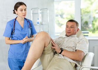 Experienced female doctor examines the sore knee of a male patient