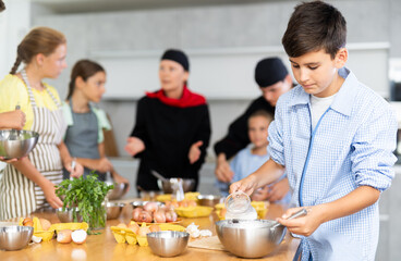 Obraz na płótnie Canvas Curious teen boy participating in culinary workshop led by professional chefs for tweens and learning how to cook..