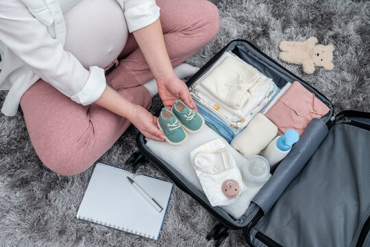 Pregnant woman's top view, floor-based preparations, packing with precision her maternity essentials, encapsulating the future mother's emotions