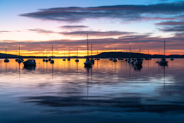 Fototapeta na wymiar Sunrise over the water with boats, reflections and high cloud