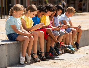 Children chatting on their smartphone, sitting on street parapet