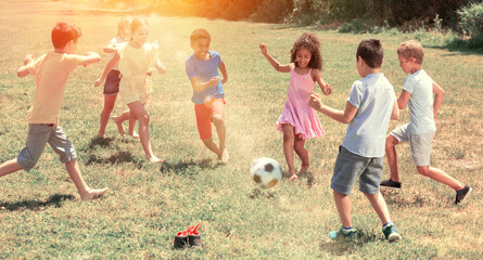 Group of happy schoolchildren playing football together in park