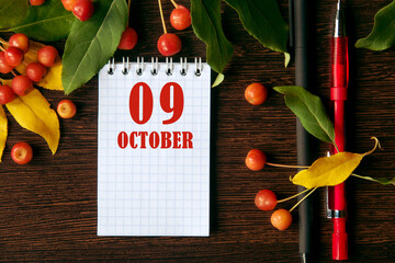 calendar date on wooden dark desktop background with autumn leaves and small apples. October 9 is...